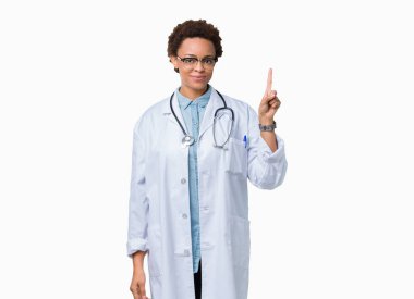 Ve parmak gülümseyen süre bir numara ile kendinden emin ve mutlu yukarıyı gösteren izole arka plan üzerinde tıbbi ceket giyen genç Afro-Amerikan doktor kadın.