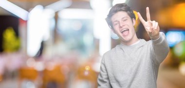 İzole arka plan üzerinde sweatshirt giyen genç yakışıklı sportif adam gösteren ve parmaklar iki numarası ile işaret kadar emin ve mutlu gülümseyen.