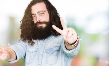 Uzun saç ve sakal gözlük kamera zafer işareti yapıyor parmak gösteren seyir gülümseyen genç hipster adam. İki numaralı.