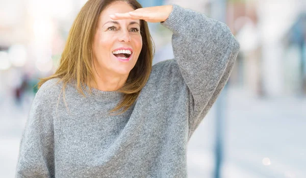 孤立した背景の上に冬のセーターを着ている美しい中年の女性は非常に幸せで 頭の上に手で遠くに見て笑顔 概念の検索 — ストック写真