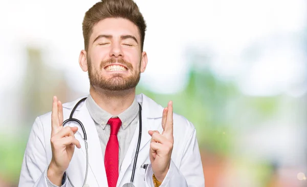 Homem Médico Bonito Jovem Vestindo Casaco Médico Sorrindo Cruzando Dedos — Fotografia de Stock