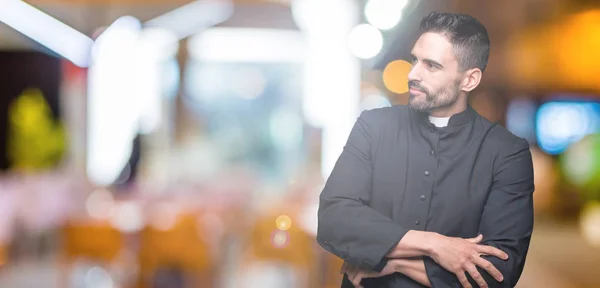 Young Christian priest over isolated background smiling looking to the side with arms crossed convinced and confident