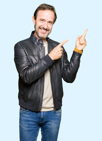 笑顔で側に つの手と指で指しているカメラ目線の黒革ジャケットを着て中年ハンサムな男 — ストック写真