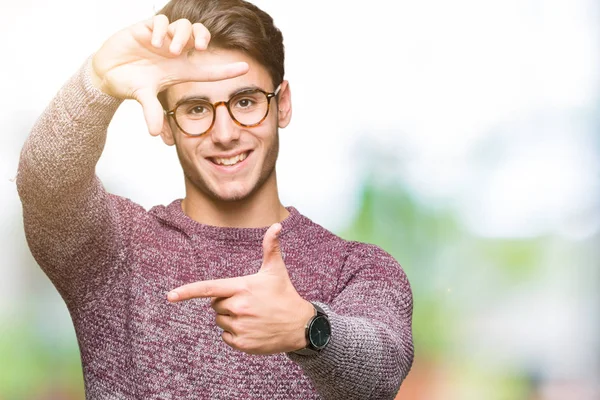 Young handsome man wearing glasses over isolated background smiling making frame with hands and fingers with happy face. Creativity and photography concept.