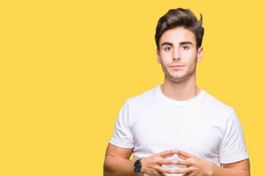 Arka plan eller üzerinde beyaz t-shirt giyen genç yakışıklı adam birlikte izole ve rahat ve neşeli gülümseyen parmak çarpı işareti. Başarı ve iyimser