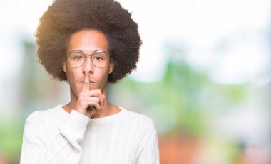 Afrikalı-Amerikalı genç afro saçlı gözlüklü dudaklarında parmak ile sessiz olmanı. Sessizlik ve gizli kavramı.
