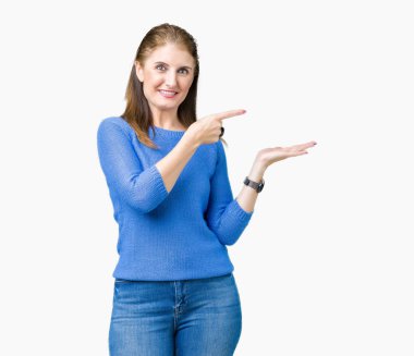 Hayret ve el ile sunulması ve parmak ile işaret ederken kameraya gülümseyen izole arka plan üzerinde kış kazak giyen güzel orta yaş Olgun kadın.