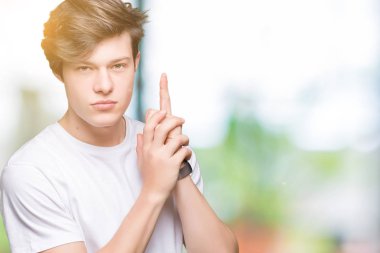 İzole arka planda rahat beyaz t-shirt giyen genç yakışıklı adam el jest ile sembolik silah tutarak, öldürme çekim silah oynarken, öfkeli yüz