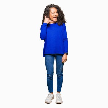 Kıvırcık saçlı kış kazak giyen genç güzel kadın telefonda konuşmak gibi el ve parmaklarla telefon hareketi yaparak gülümsüyor. İletişim kavramları.