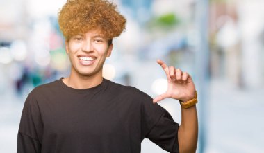 Siyah t-shirt gülümseyen ve süre seyir ve kamera boyutu işaret parmaklarıyla yapıyor el ile kendine güvenen el hareketi afro saçlı genç yakışıklı adam. Ölçü kavramı.