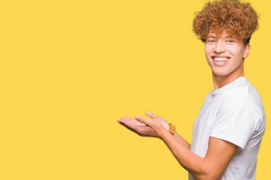 Genç yakışıklı adam ile afro saç giyen Casual beyaz t-shirt el ve açık palmiye ile yan Işaret, reklam gülümseyen mutlu ve emin sunan