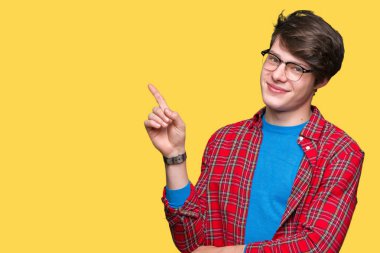 Yüzünde kocaman bir gülümseme ile izole arka plan üzerinde gözlük takan genç yakışıklı öğrenci adam kameraya bakarak yan el ve parmak ile işaret.