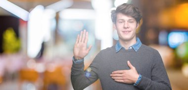 Genç yakışıklı zarif adam izole arka plan üzerinde göğüs ve bir sadakat sözü yemin yapma avuç, el ile küfür