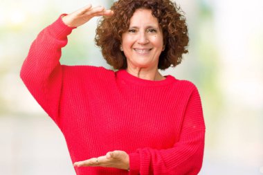 Güzel orta ager üst düzey kadın kırmızı kış kazak üzerinde arka plan ile büyük ve büyük boy işaret, ölçü birimi sembol gösteren el eller izole. Kameraya bakarak gülümsüyordu. Ölçüm kavramı.