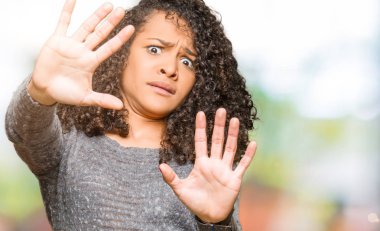 Gri kazak giyen kıvırcık saçlı Genç güzel kadın korkuyor ve korku ifadesi ile korkmuş el, şok bağırarak jest durdurmak. Panik konsepti.