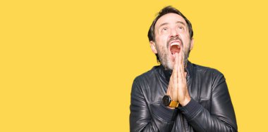 Orta Çağ yakışıklı adam siyah deri ceket giyerek yalvarıyor ve el ile birlikte dua yüz üzerinde umut ifade ile çok duygusal ve endişeli. Affedilmesini istiyorum. Din konsepti.