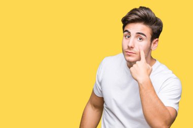 Beyaz t-shirt üzerinde izole giyen genç yakışıklı adam arka plan işaret jest göz izlemek için şüpheli ifade