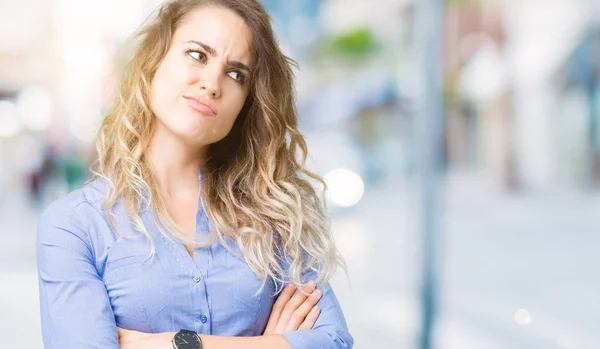 Beautiful young blonde business woman over isolated background smiling looking to the side with arms crossed convinced and confident