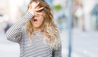 Giyen genç güzel sarışın kadın kazak yüz ve gözler el ile kapsayan şok bakmak izole arka plan üzerinde parmak utanç ifadesi ile bakarak çizgili.