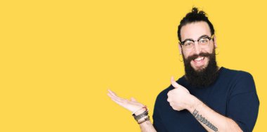 Genç hipster adamım uzun saç ve sakal gözlük ile gösteren palm el ve iş tamam jestle başparmak, mutlu ve neşeli gülümseyen