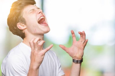 Yakışıklı delikanlı deli ve silah ile başarı için deli kutluyor izole arka plan üzerinde rahat beyaz t-shirt giyen kaldırdı ve heyecanlı çığlık gözler kapalı. Kazanan kavramı