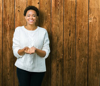 Güzel genç Afro-Amerikan kadın giyiyor kazak izole üzerinden alma veya jest vererek birlikte el avuç içi ile gülen arka plan. Ayrı tutma ve koruma