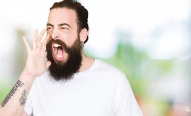 Uzun saç ve sakal bağırarak ve ağzı üzerinde el ile yan için çığlık casual beyaz t-shirt giyen genç hipster adam. İletişim kavramı.