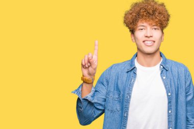 Afro saçlı kot ceket gösterme ve kendinden emin ve mutlu gülümseyen bir parmak ile işaret eden oktan yukarı giyen genç yakışıklı adam.