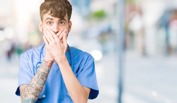 Young handsome nurse man wearing surgeon uniform over isolated background shocked covering mouth with hands for mistake. Secret concept.