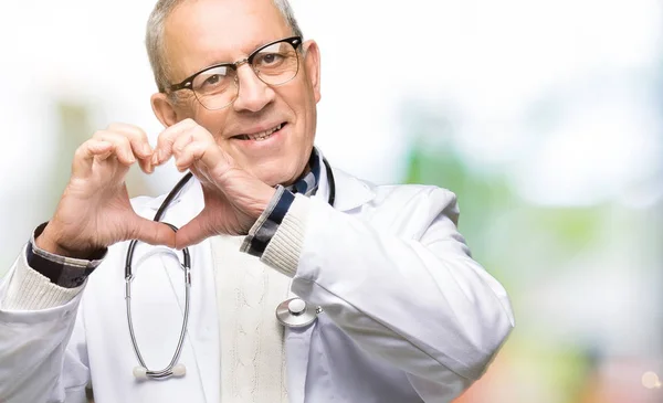 ハンサムな先輩医師男恋ハートマークと手で形を示す笑みを浮かべて医療のコートを着ています ロマンチックな概念 — ストック写真
