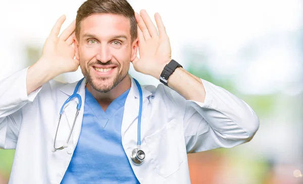 英俊的医生穿着医疗制服在孤立的背景试图听到双手对耳朵的手势 好奇八卦 听力问题 — 图库照片