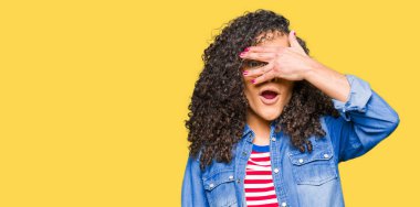 Mahcup ifadeyle parmaklarımın arasından arayan genç güzel kadın kıvırcık saçlı gözlüklü yüz ve gözler el ile kapsayan şok bakmak.