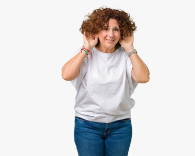 Her iki kulak jest, dedikodu için meraklı ellerde dinliyoruz izole arka plan üzerinde beyaz t-shirt giyen güzel orta ager kadın kıdemli. İşitme sorunu, sağır