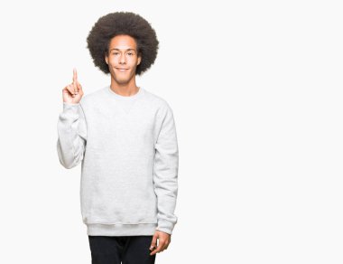 Sportif kazak gösterme ve kendinden emin ve mutlu gülümseyen bir parmak ile işaret eden oktan yukarı giyen afro saçlı genç Afro-Amerikan adam.