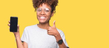 İzole arka plan üzerinde Smartphone ekran ok işareti, başparmak ile parmak, mükemmel işareti yapıyor kocaman bir gülümseme ile mutlu gösteren genç Afro-Amerikan kadın
