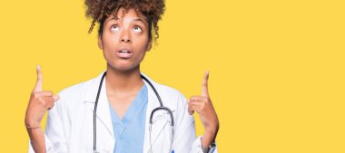 Genç Afro-Amerikan doktor kadın izole arka plan üzerinden hayran ve yukarıya bakıp parmakları ile işaret şaşırttı ve silah kaldırdı.