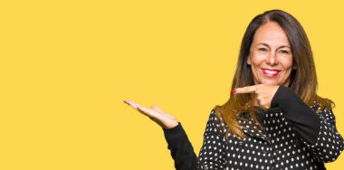 Hayret ve el ile sunulması ve parmak ile işaret ederken kameraya gülümseyen moda ceket giyen güzel orta yaş kadın.