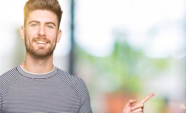 Kameraya bakarak yan el ve parmak ile işaret yüzünde kocaman bir gülümseme ile kazak giyen genç yakışıklı adam çizgili.