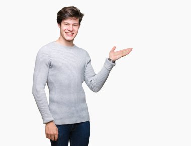 Neşeli sunulması ve kameraya bakarak avucunun ile işaret gülümseyen izole arka plan üzerinde kış kazak giyen genç yakışıklı adam.