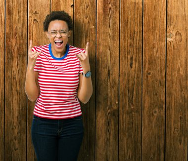 Deli ifade rock simge elle yapıyor ile bağırarak izole arka plan üzerinde gözlük güzel genç Afro-Amerikan kadın. Müzik yıldızı. Ağır kavramı.