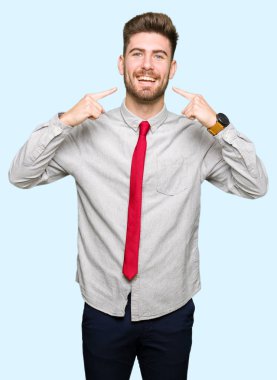 Kendinden emin gösterilen ve işaret parmakları diş ve ağız ile gülümseyen genç yakışıklı iş adamı. Sağlık kavramı.