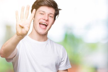 Yakışıklı delikanlı gösterilen ve parmakları ile işaret izole arka plan üzerinde rahat beyaz t-shirt giyen süre kendinden emin ve mutlu gülümseyerek dört numara.