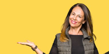 Gülen iki elle gösterilen avuç içi, sunma ve karşılaştırma ve denge reklam açık kış yelek giyen güzel orta yaş kadın