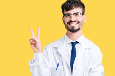 Mutlu yüz zafer işareti yaparken kameraya göz kırpıyor ile gülümseyen izole arka plan üzerinde Beyaz önlük giyen genç profesyonel bilim adamı. İki numaralı.
