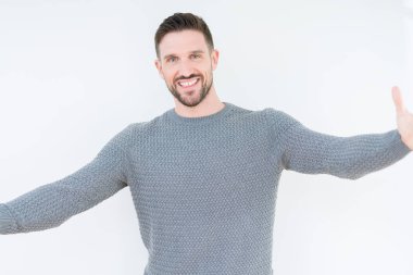 Genç yakışıklı adam kucaklamak için açık kollar ile gülümseyen kamera bakıyor izole arka plan üzerinde Casual kazak giyiyor. Mutluluğu kucaklayan neşeli ifade.