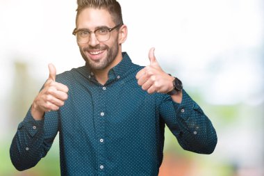 Genç yakışıklı iş adamı izole arka plan başarı işareti el ile pozitif jest yapıyor üzerinde gözlük takan başparmak gülümseyen ve mutlu. Neşeli bir ifadeyle, kazanan jest kameraya bakıyor.