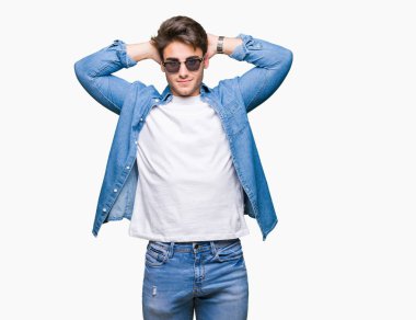 Genç yakışıklı adam giyen güneş gözlüğü izole üzerinde arka plan dinlenirken ve germe kollar ve eller baş ve boyun arkasında ile mutlu gülümseyerek