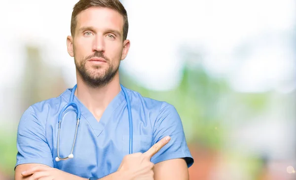 英俊的医生穿医疗制服在孤立的背景指向侧用手指显示广告 严肃和平静的脸 — 图库照片