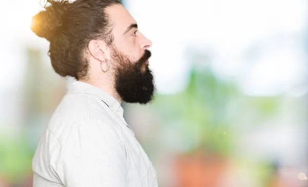 Young man with long hair, beard and earrings looking to side, relax profile pose with natural face with confident smile.