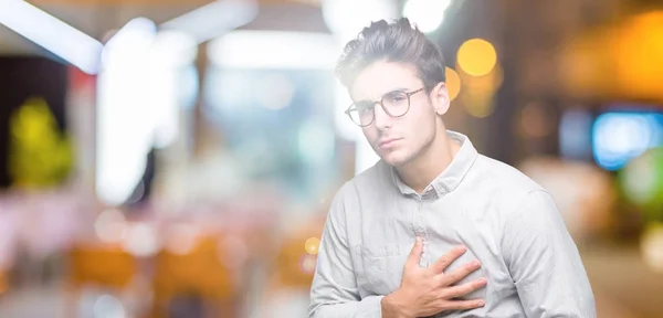 Young handsome man wearing glasses over isolated background with hand on stomach because indigestion, painful illness feeling unwell. Ache concept.